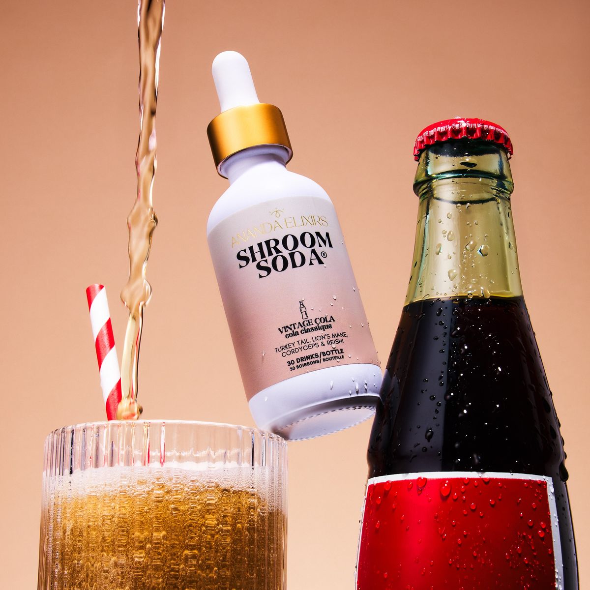 A Shroom Soda bottle beside a glass of poured amber soda on a peach backdrop
