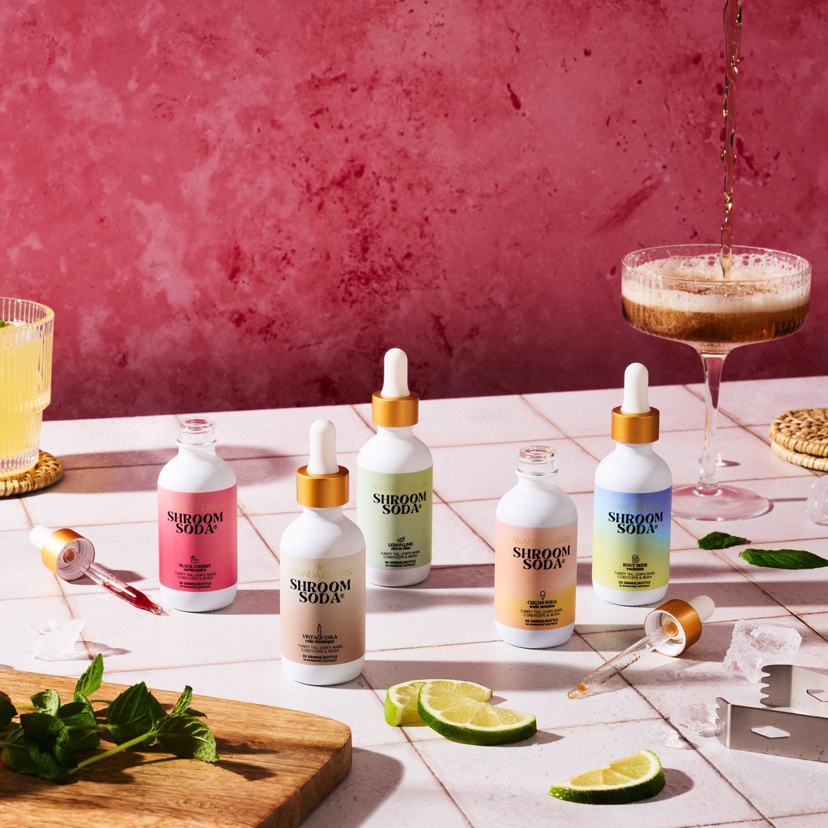 Five Shroom Soda bottles on a pink tiled table with lime, mint and a coupe glass