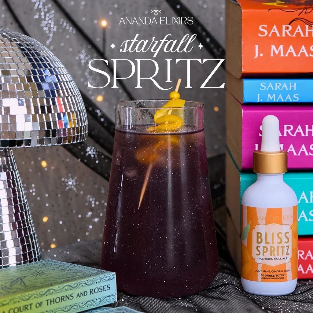 A tall glass of purple starfall spritz next to a bottle of Bliss Spritz.