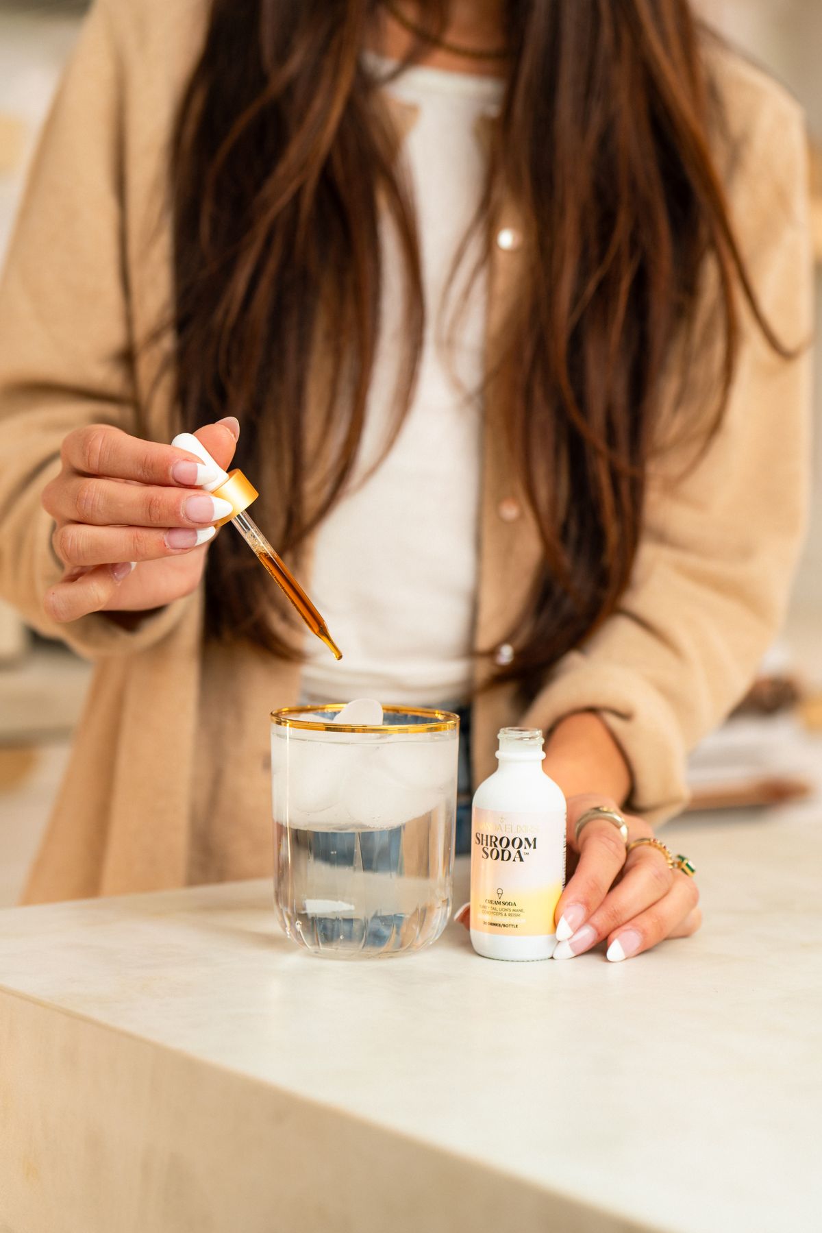 A woman drops Shroom Soda into a glass of ice and water on a marble counter